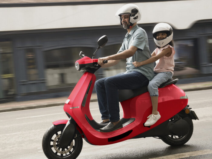 Man riding a red Ola S1 scooter with his daughter sitting pillion